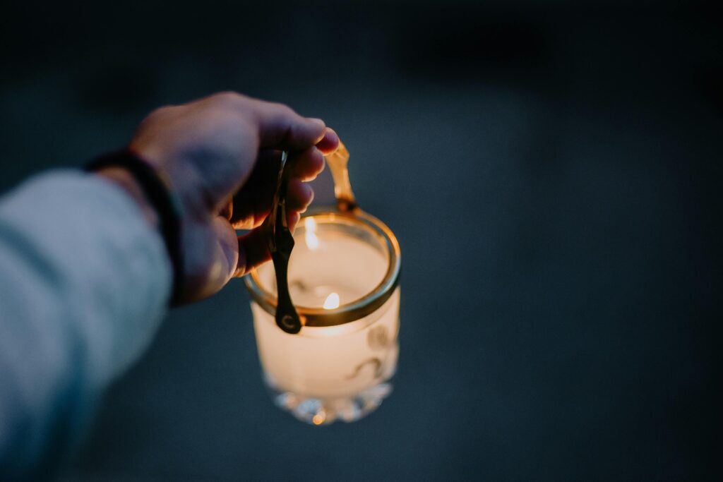 Hand holding a glowing candle lantern at dusk, representing a nightly release ritual for children