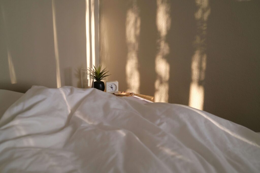 Soft golden light entering a peaceful bedroom with white sheets, symbolizing a calm morning ritual