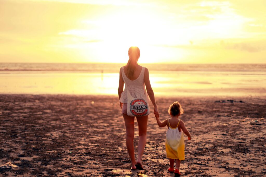 Mother and young child walking hand-in-hand on the beach at sunset, symbolizing soulful connection and daily rhythms for families