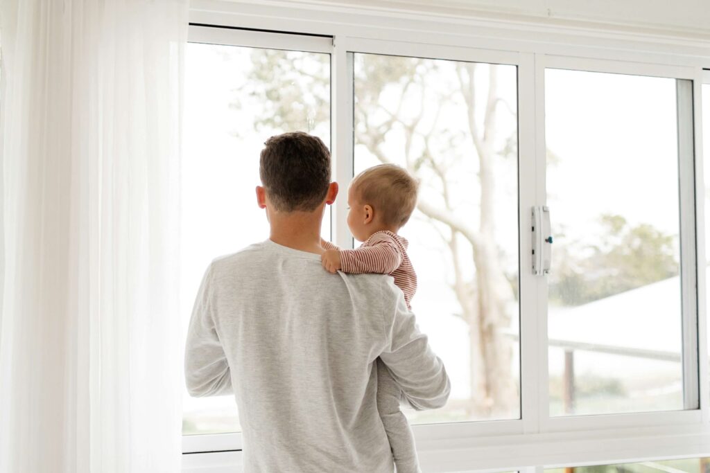 Parent and baby gazing out a sunlit window together, beginning the day with presence and connection showing daily rhythms for families
