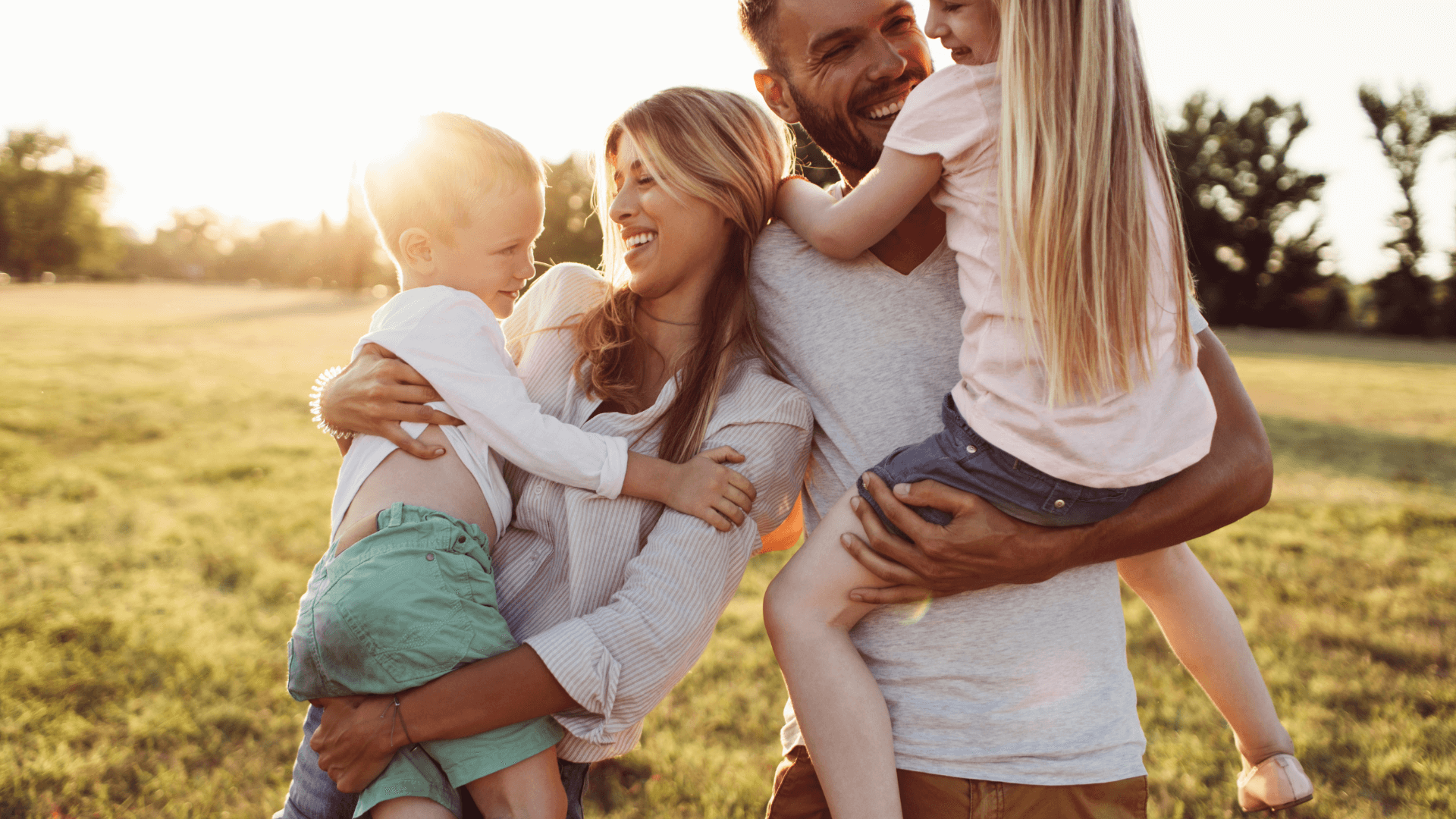 Little Guru & Co. blog family of four laughing and holding children in a sunlit field symbolizing love and connection