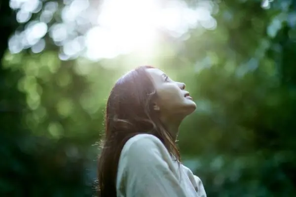 Woman standing outdoors looking up to the sky, pausing in awe and reconnecting with wonder.